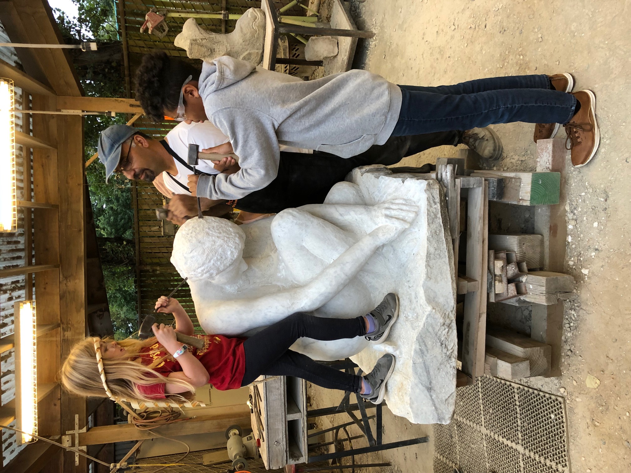 Sabah Al Dhaher, carving with kids in the Stone Yard at Pratt Fine Arts Center