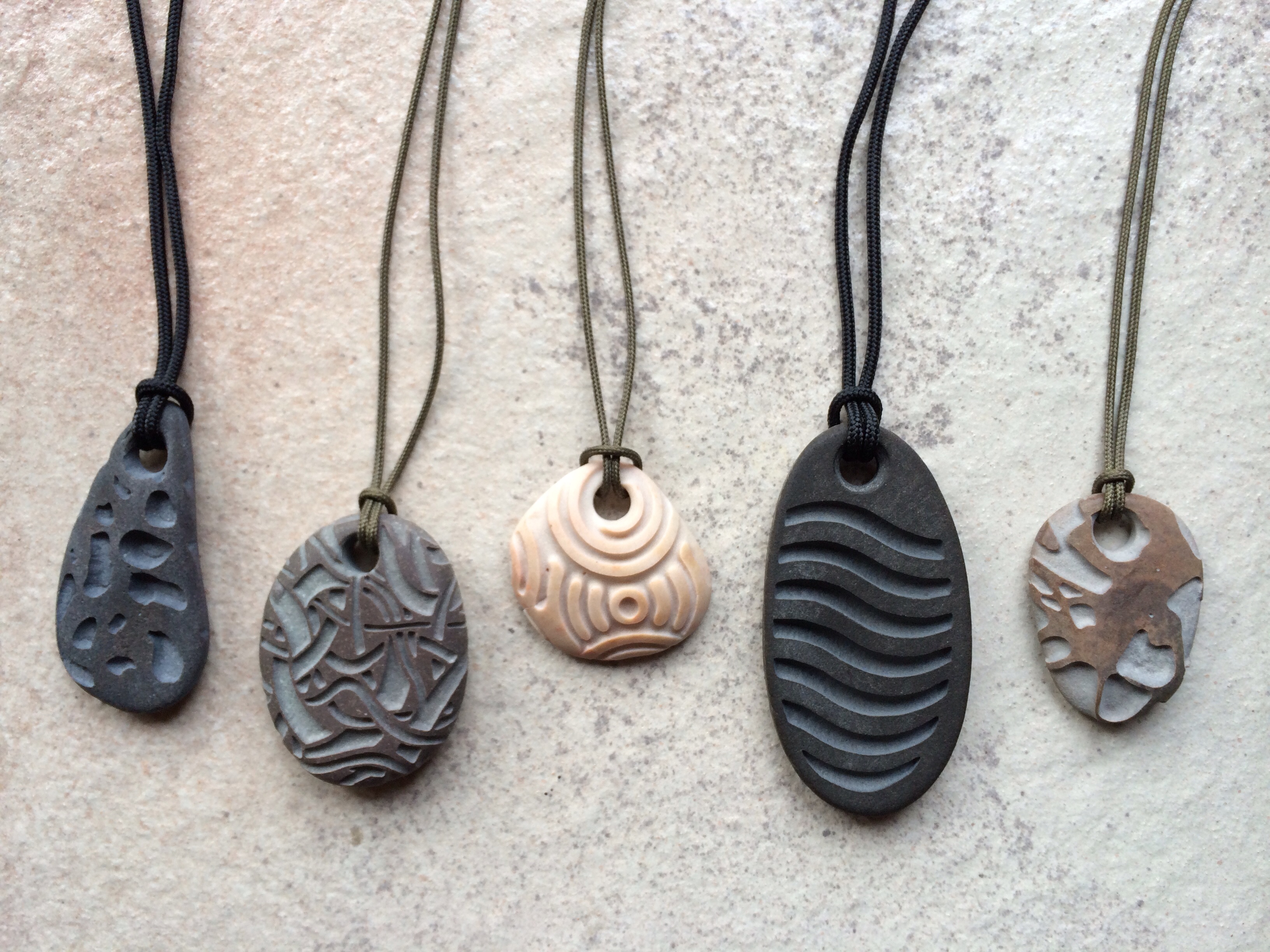 Pendants, after coring a hole for the pendant cord, I place a template over each stone and sandblast a specific design. Most are basalt, 1" to 2" long. 