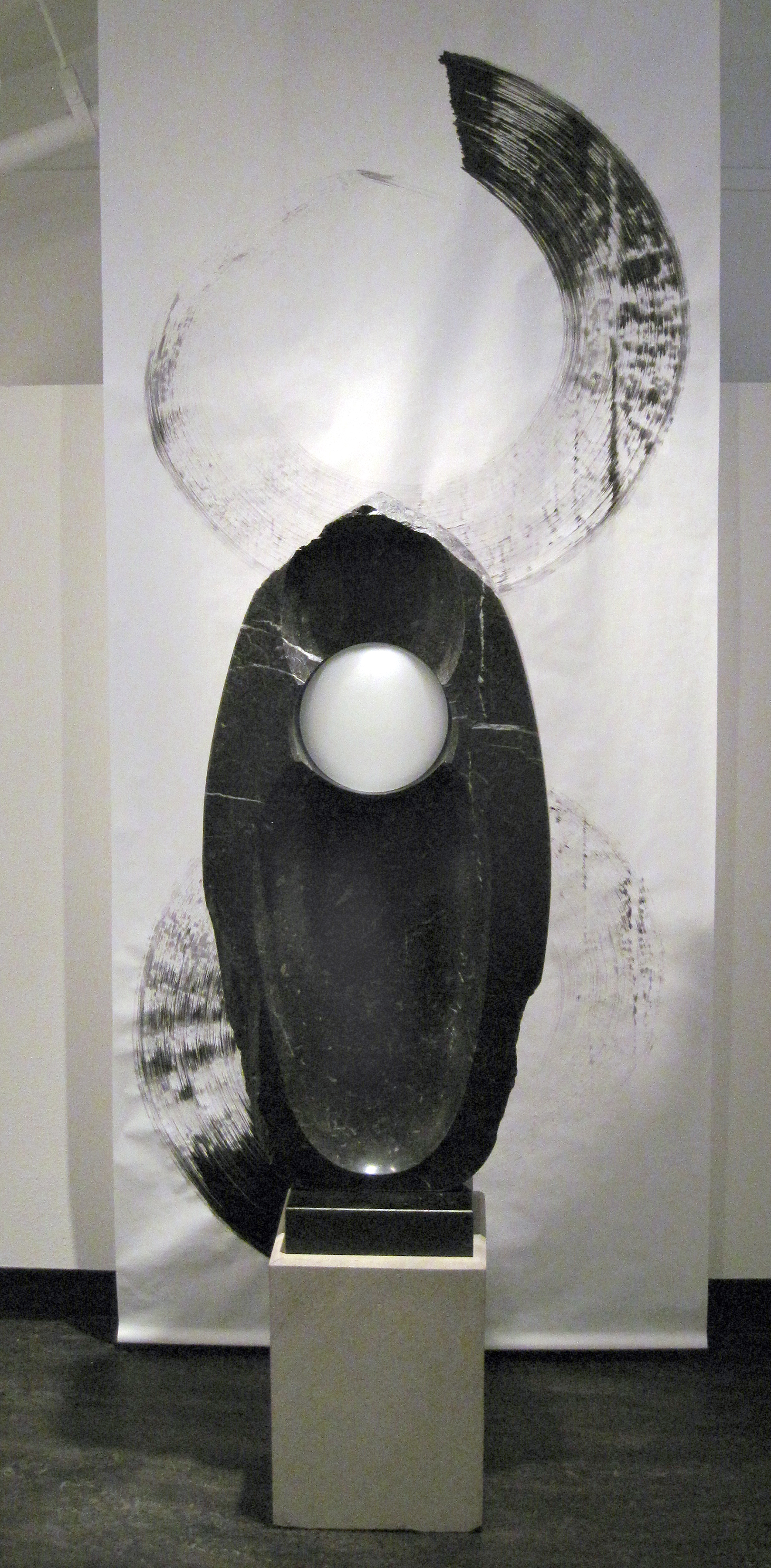 “Black Water Lens” – Chrysalis, Alaska black fossiliferous limestone, 48” X 22” X 7.” Displayed in front of a sumi-e ink painting by Jim Ballard. 